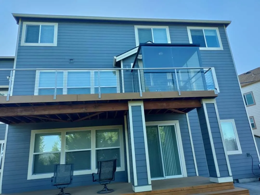 Three-story home painted steel blue with white trim and a glass balcony