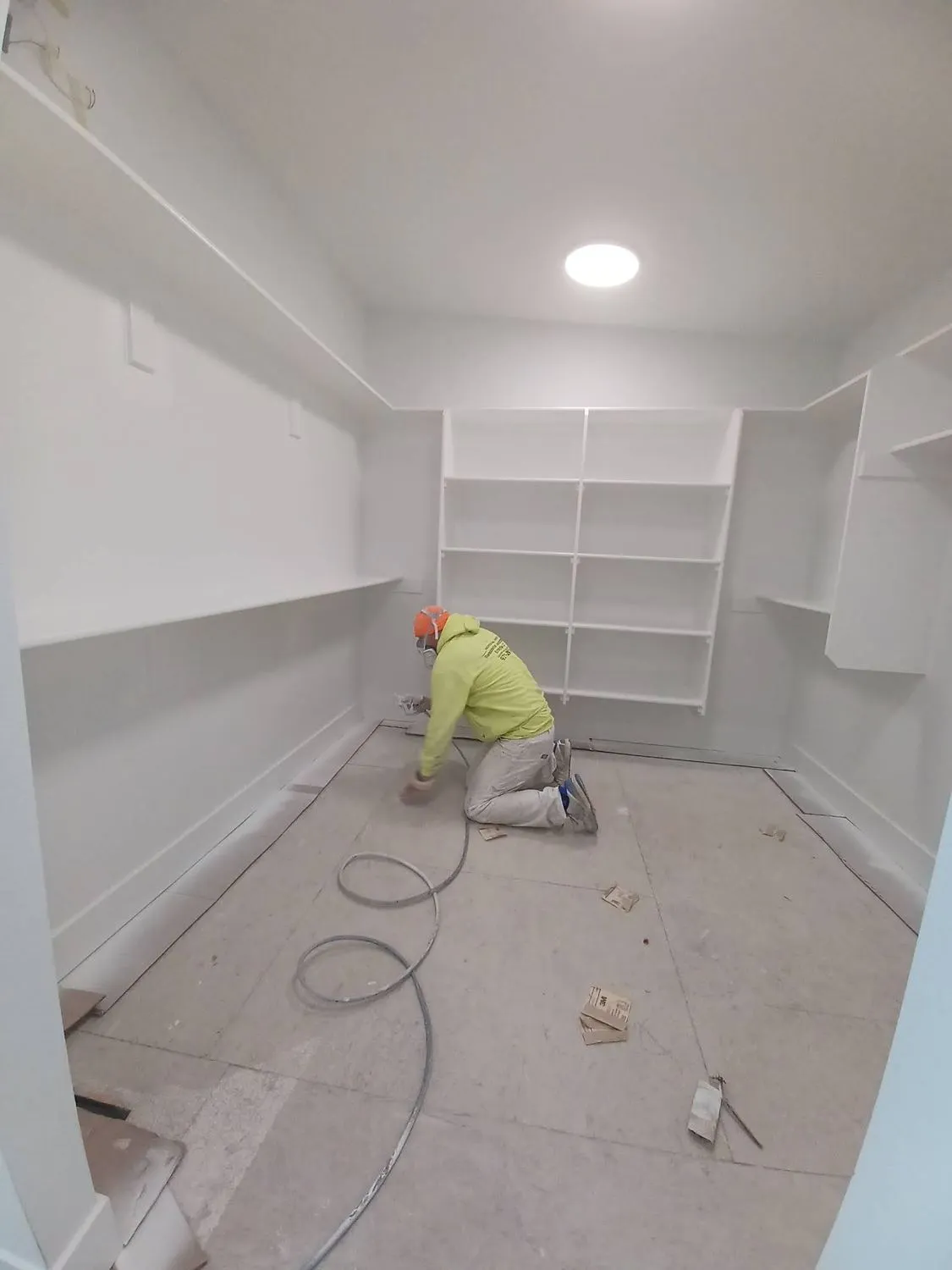 Painter spraying white built-in shelving inside a closet